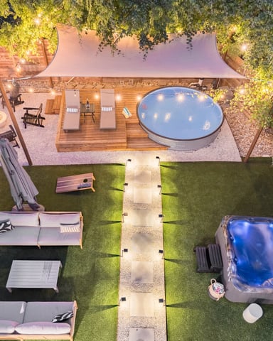 Overhead view of illuminated backyard with two hot tubs, lounge seating, wooden deck, and ivy-covered fences at dusk
